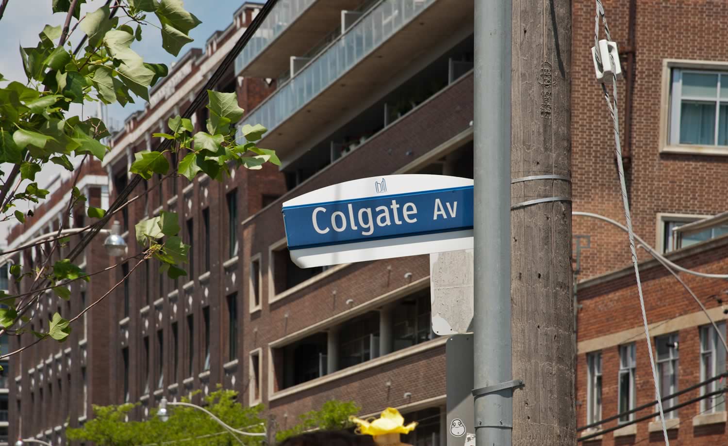 Street sign for Colgate Ave stands in front of a low brick building that has a faded paint sign over the entrance that reads 'Rolph Clark Stone.'