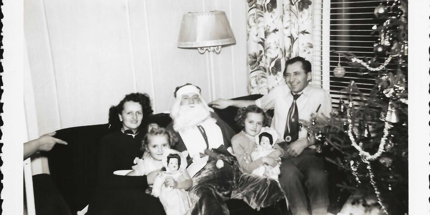Black and white image Bandura family sitting on a couch. Their uncle dressed as Santa is in the centre, with a child on either side of him. The mother is sitting to the left, their father to the right.