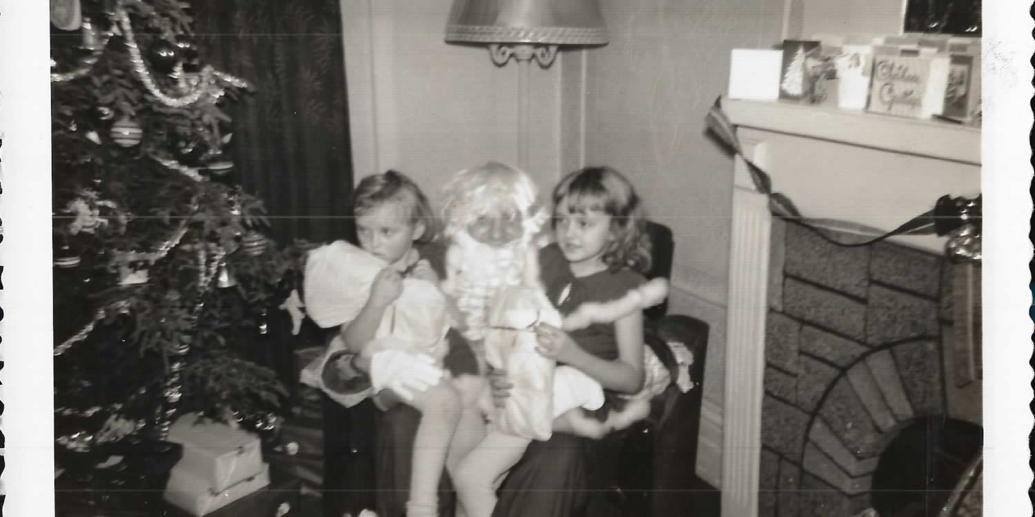 Black and white image of two young girls sitting in a living room on Santa's lap.