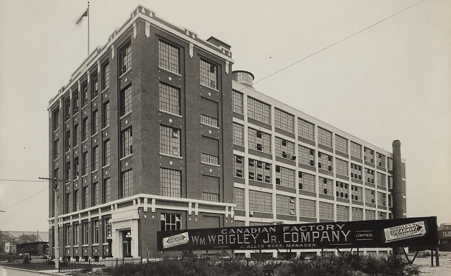 Black and white image of five-storey factory with large windows. A large sign beside the building reads: 'Canadian Factory: Wm. Wrigley Jr. Company, J. Allan Ross, manager'.