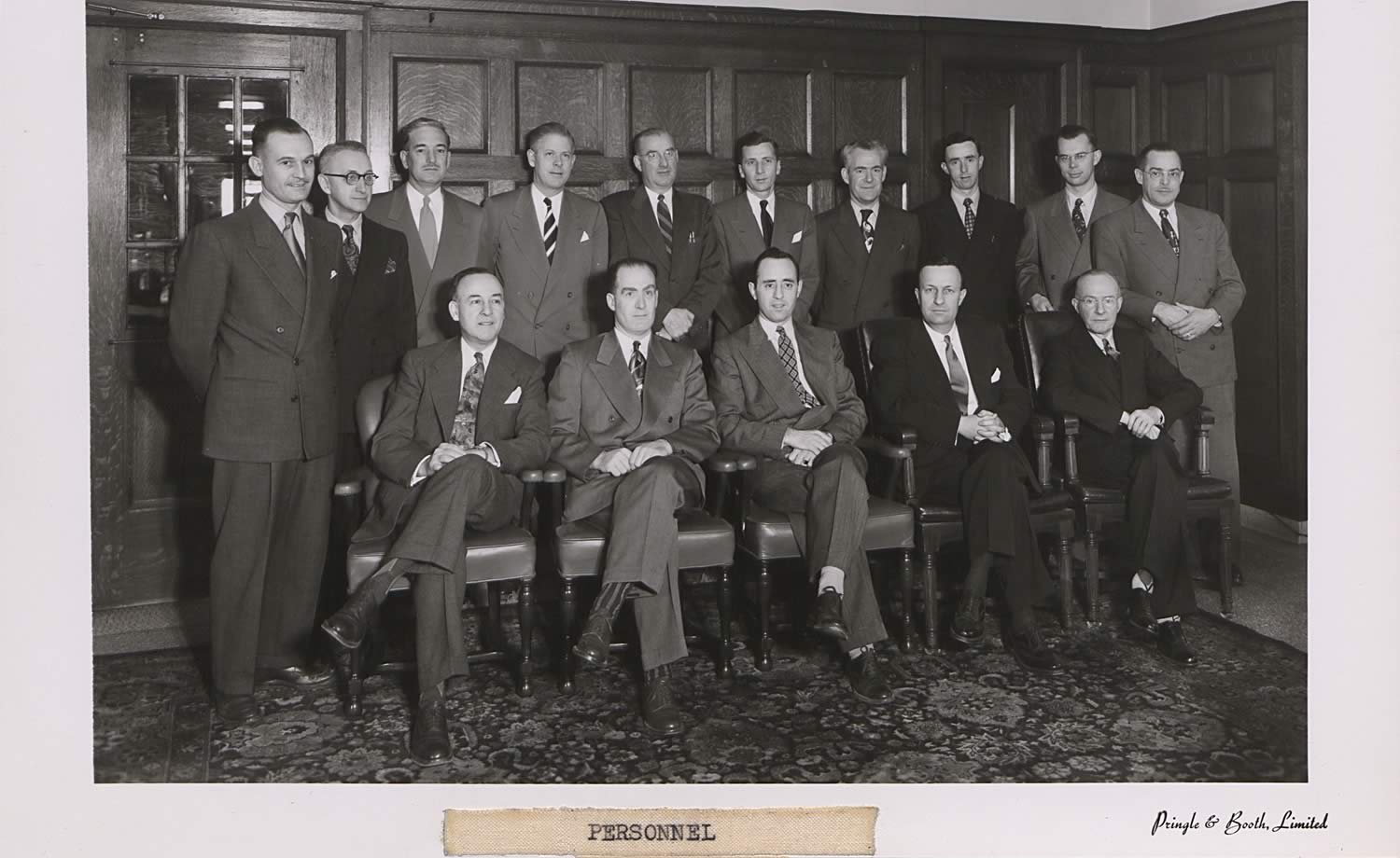Formal black and white photograph a group of men. All the men are dressed in suits; the first row are seated, the second row are standing behind them.