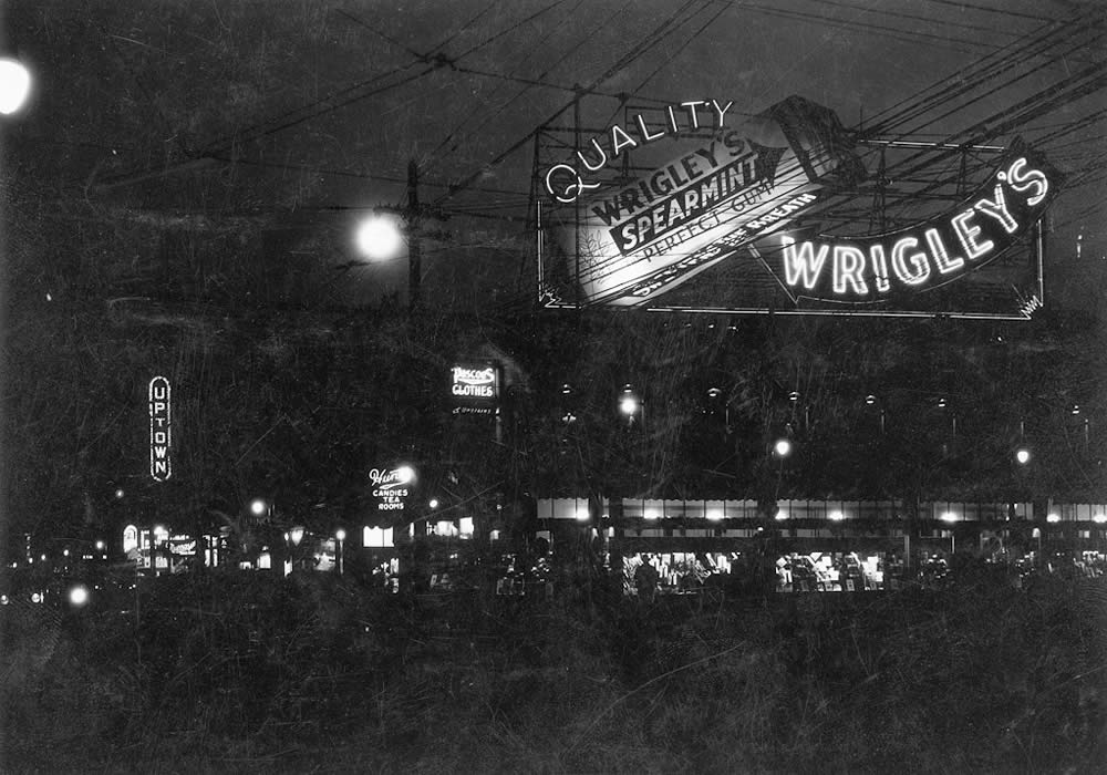 Black and white night photograph of a large neon sign advertising Wrigley's Spearmint gum at Yonge and Bloor Streets in Toronto, looking south. The marquee of the Uptown movie theatre is visible in the background.