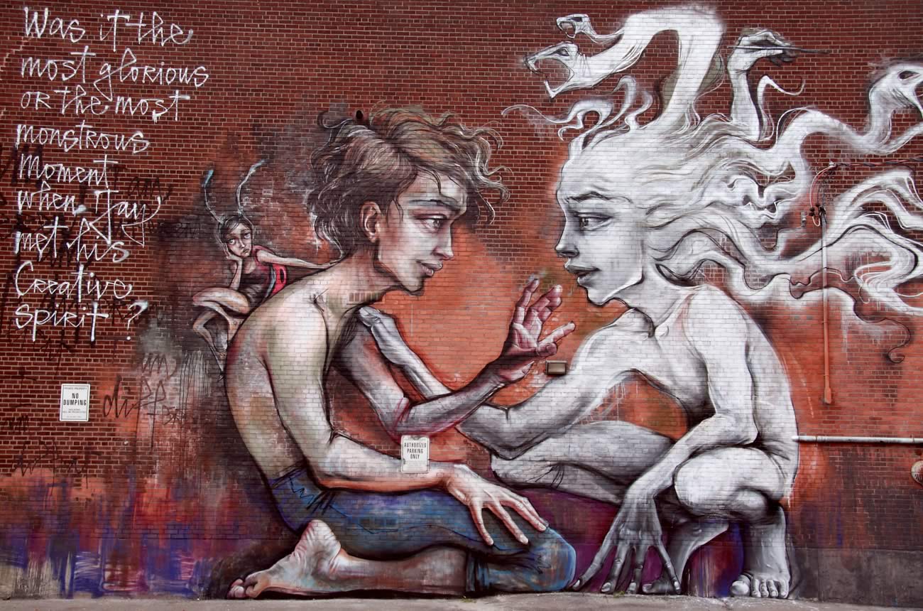 Colour image of a mural on a large brick building. The mural represents two figures kneeling and talking to each other. The one of the left is bare chested and wearing jeans; the other is a white ghostly figure. On the left top corner, is the sentence 'Was it the most glorious or the most monstrous moment when Jay met his creative spirit?'