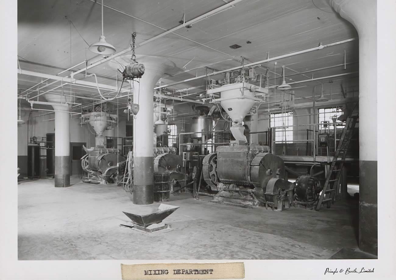 Black and white photograph of large room. Three identical machines in the room for mixing; the machines are floor to ceiling. There is a white substance covering most of the open floor space.