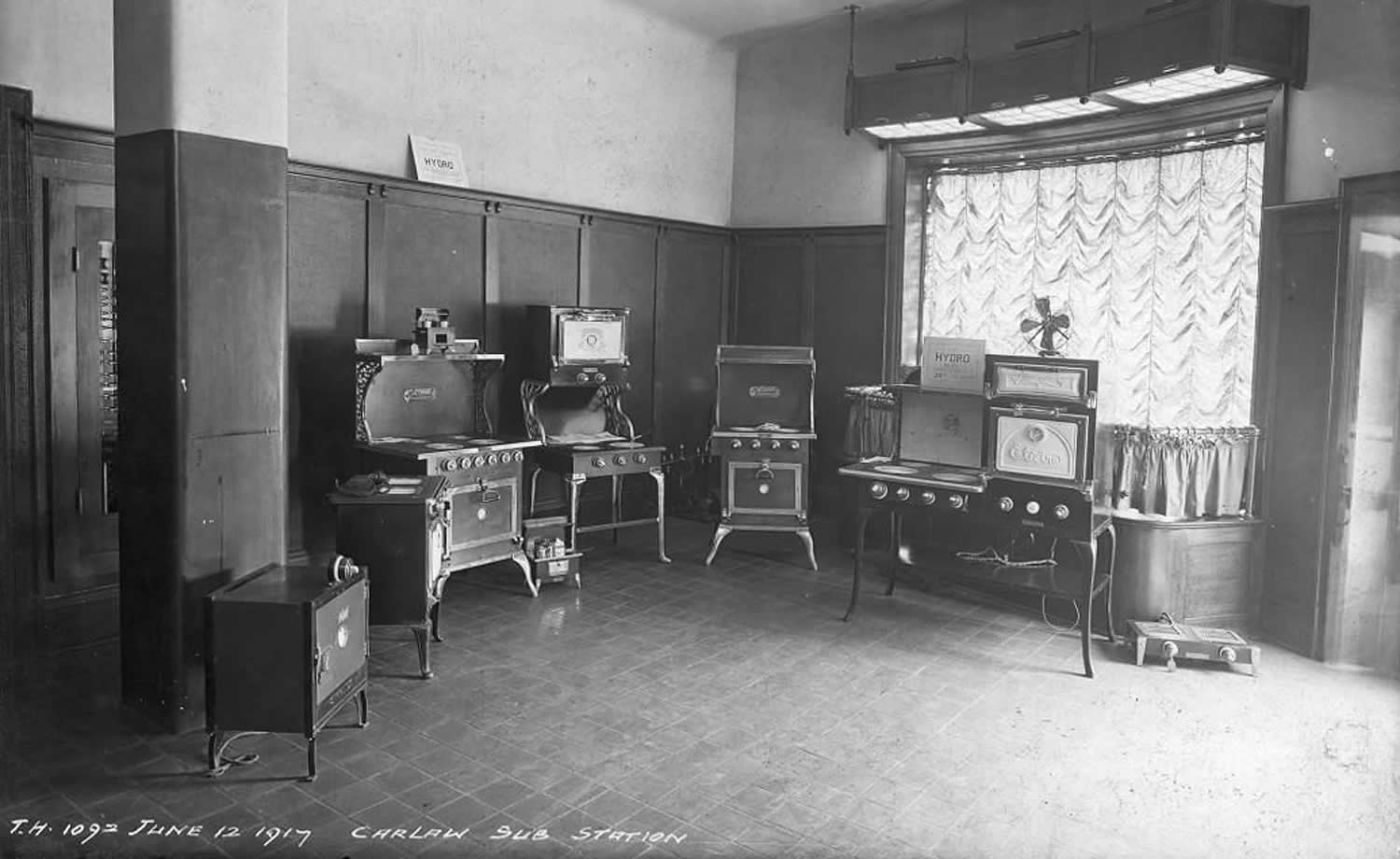 Black and white photograph of a store with early electric stoves on display.